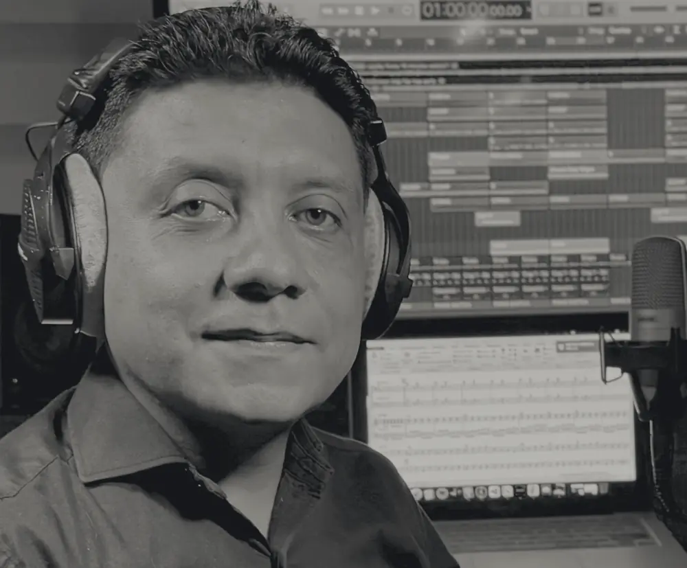 Julián Guacaneme con audífonos en su estudio, frente a una sesión de producción y una partitura